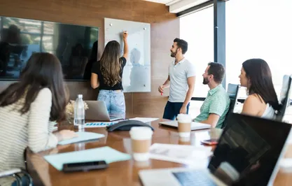 Groupe en formation sur-mesure en préparation mentale Méthode TARGET®, avec un intervenant et des participants échangeant autour d’un tableau.