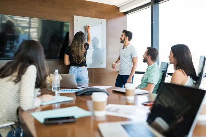 Groupe en formation sur-mesure en préparation mentale Méthode TARGET®, avec un intervenant et des participants échangeant autour d’un tableau.